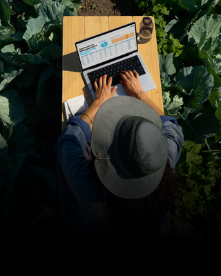 日の当たる屋外のテーブルで、電源につないでいないシルバーの14インチMacBook Proで作業をしている人物